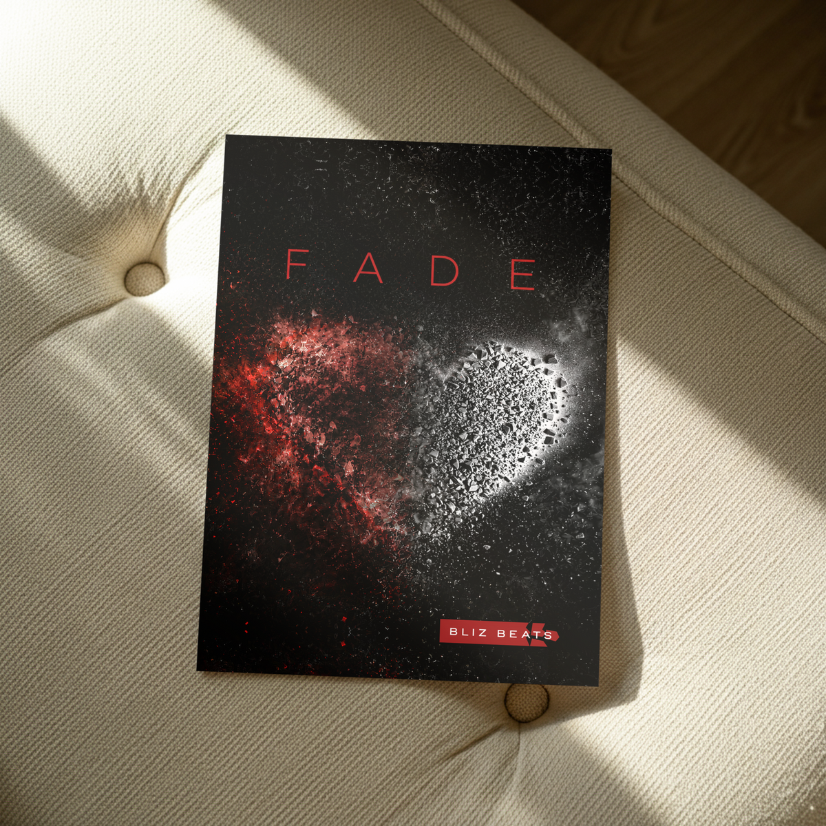 A poster rendering titled "FADE" with a dark cover design, placed on a cream tufted chair in sunlight. The cover shows a red-and-white heart-like abstract graphic and the brand name "BLIZ BEATS" at the bottom.
